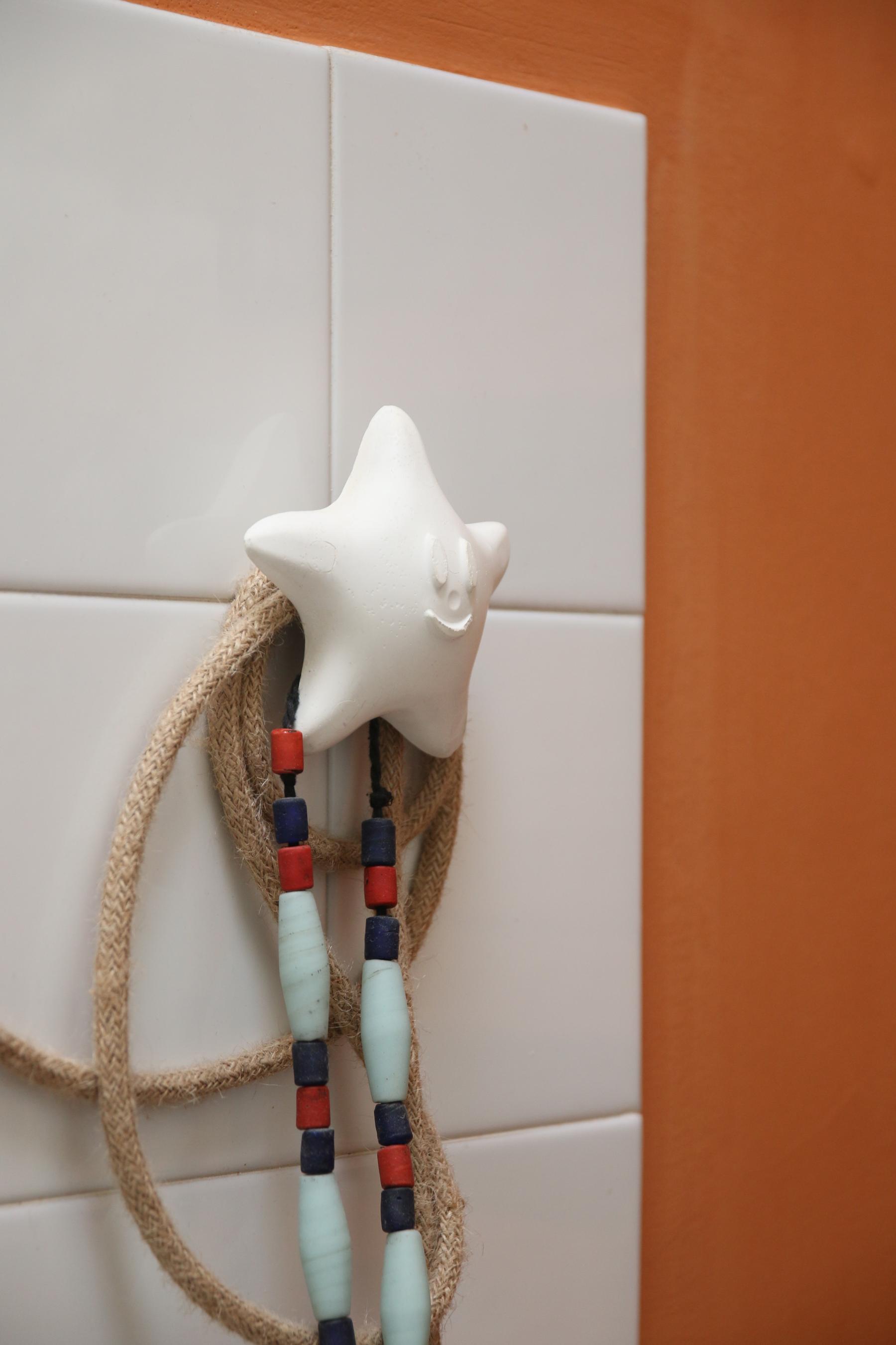Détail sur une patère design by Jérôme Barrier en plâtre sur lequel sont accrochés un collier et le câble de la lampe baladeuse en corde tressé dans la salle de bain sur mesure à Vertou imaginée par Jérôme Barrier.
